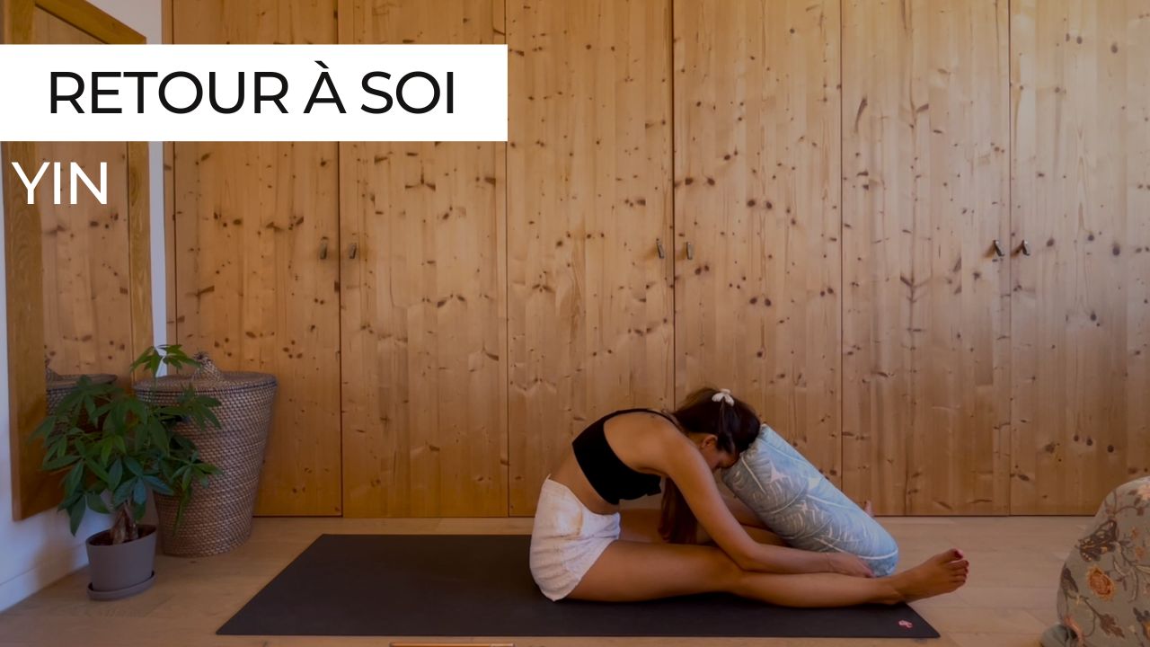 Femme en posture de pince assise (Paschimottanasana) avec un bolster sous son torse, dans un cadre calme et apaisant.