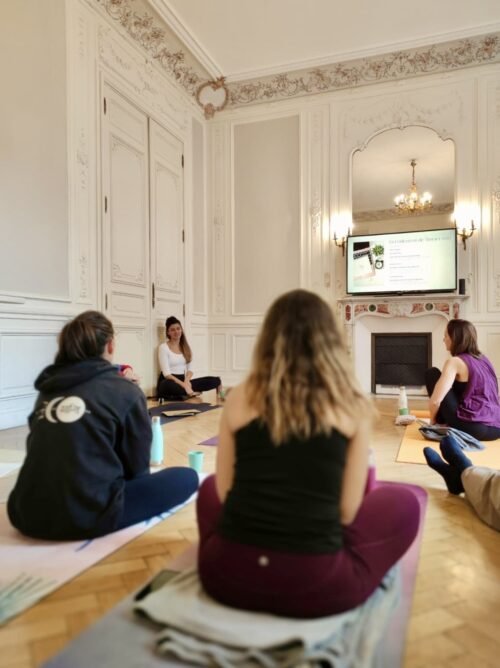 Marie enseignant à un groupe de professeurs de yoga lors de l'immersion de la formation, dans une belle salle de pratique.